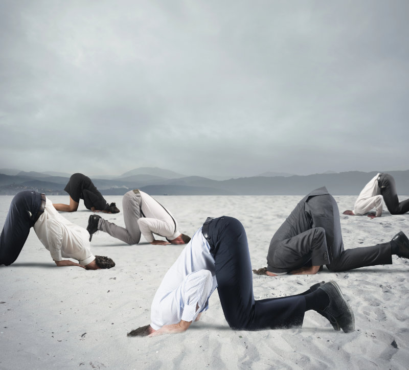 Heads buried in sand Six kneeling businesspersons with their heads buried in sand