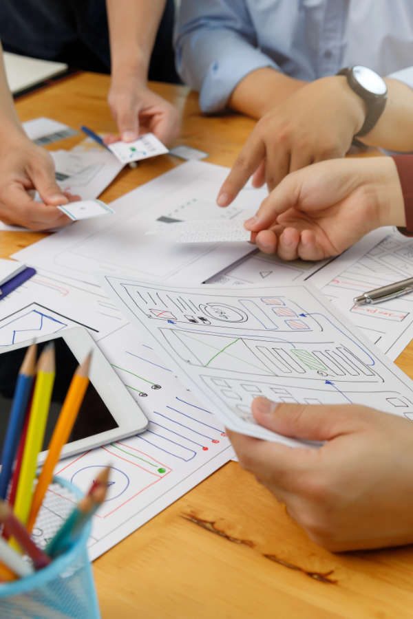 People engaged in a project discussion, surrounded by papers and pencils on a table.